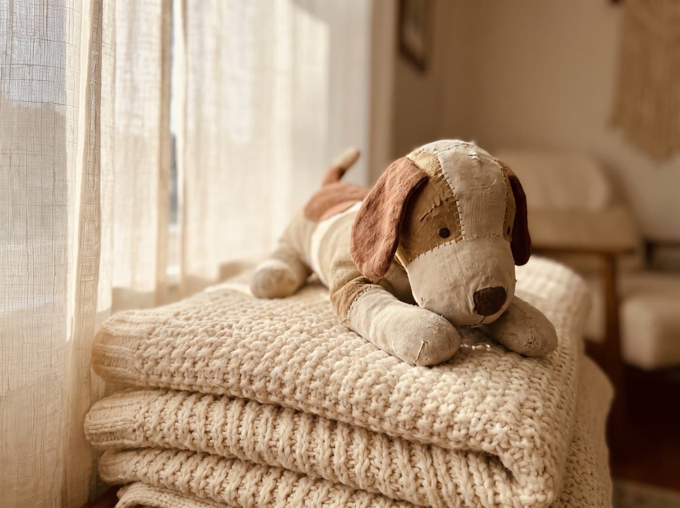 A hand-sewn plush dog resting on a soft cream blanket in warm light